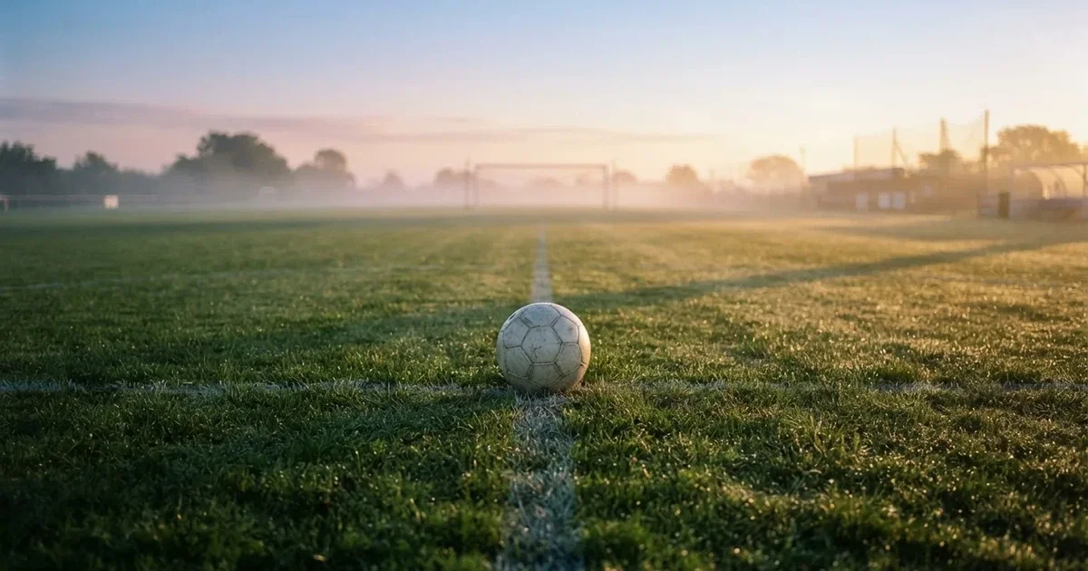 Een voetbal op de middenstip van een grasveld in het ochtendlicht